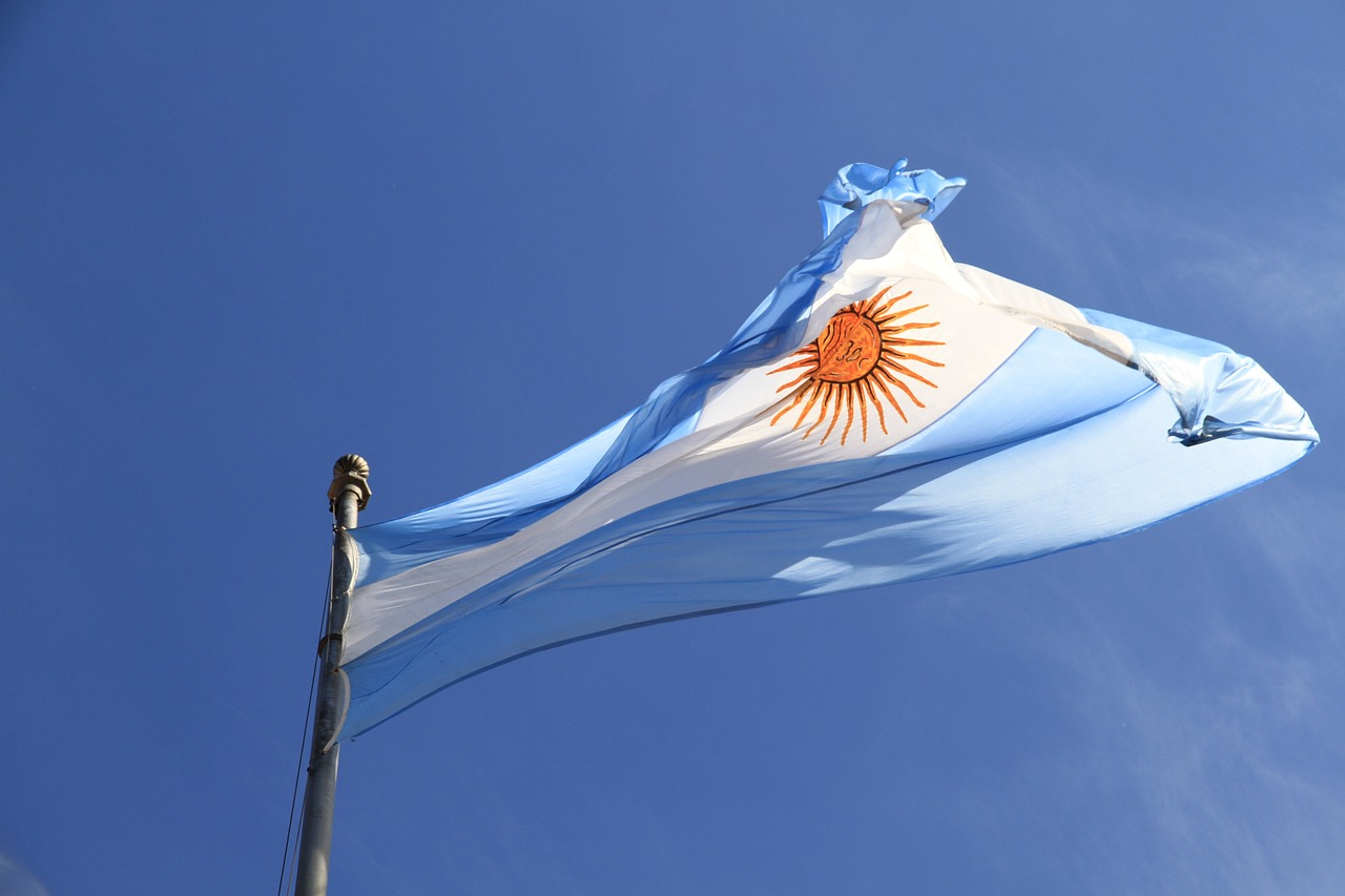 Bandera argentina ondeando contra un cielo azul, representando la democracia y resiliencia de Argentina en la era contemporánea.
