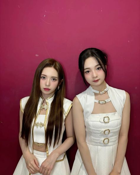 This  contain an image of 143 Entertainment  standing next to each other in front of a pink wall wearing white dresses