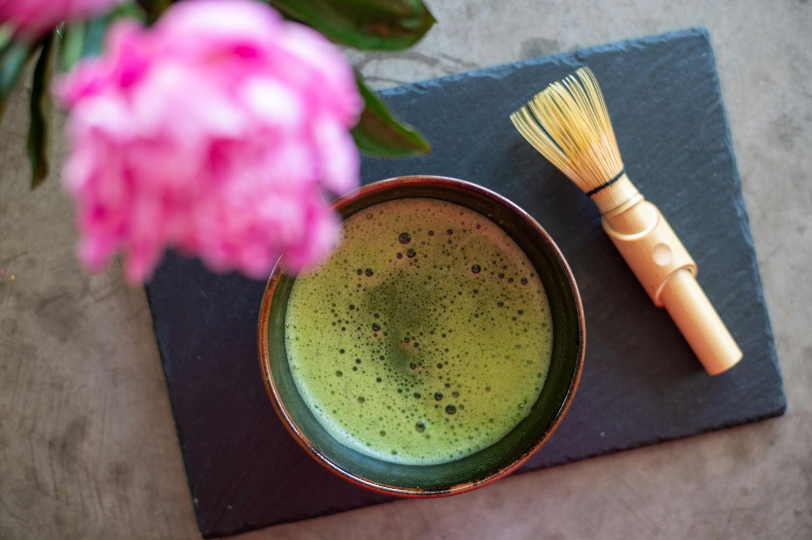 A bowl of matcha tea accompanied by a brush on a table