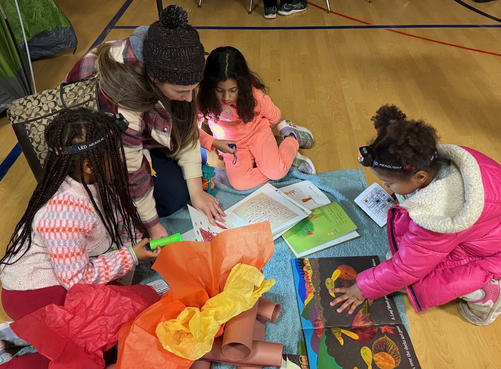 Three elementary age students read books together with a teacher on the gym floor at Bonnie Brae Elementary School. 