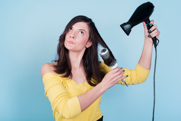 Brunette girl drying her hair using Hair Dryer and Comb