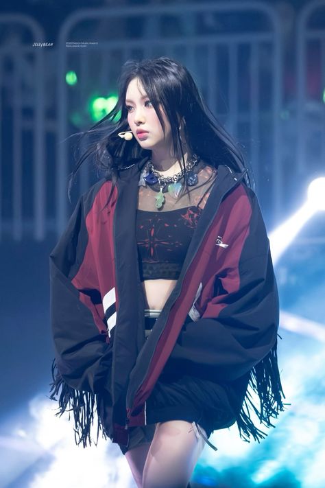 This contains an image of Hyein walking down a runway wearing a black and red jacket with fringes on it