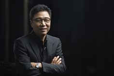 This contains an image of Lee Soo Man's in a black suit and glasses with his arms crossed