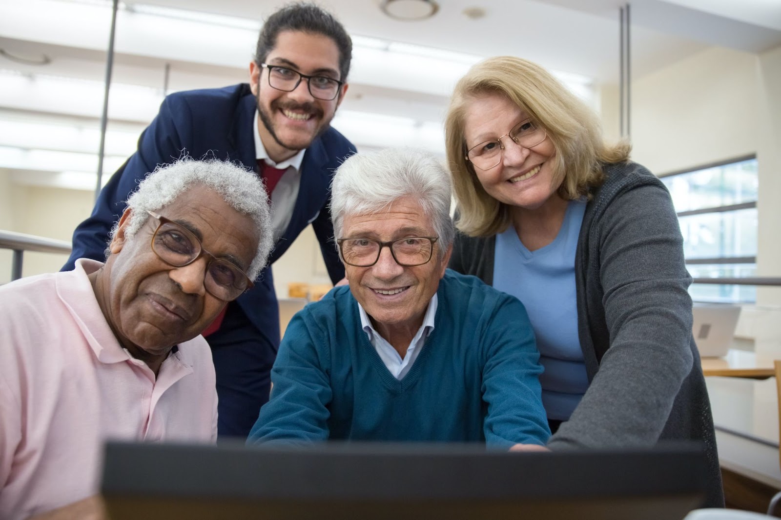 People of different ages standing behind the screen of a laptop computer while smiling