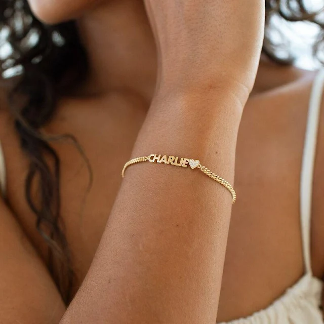 Custom Gold Name Bracelet with Pave Heart Detail Personalized gold name bracelet with a 'CHARLIE' nameplate and a small, glittering heart accent, worn on a wrist. This dainty custom jewelry piece is perfect for daily wear or as a meaningful gift.