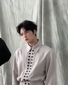 This contain Kim Jaejoong  wearing glasses and a shirt with polka dots on it, standing in front of a white curtain