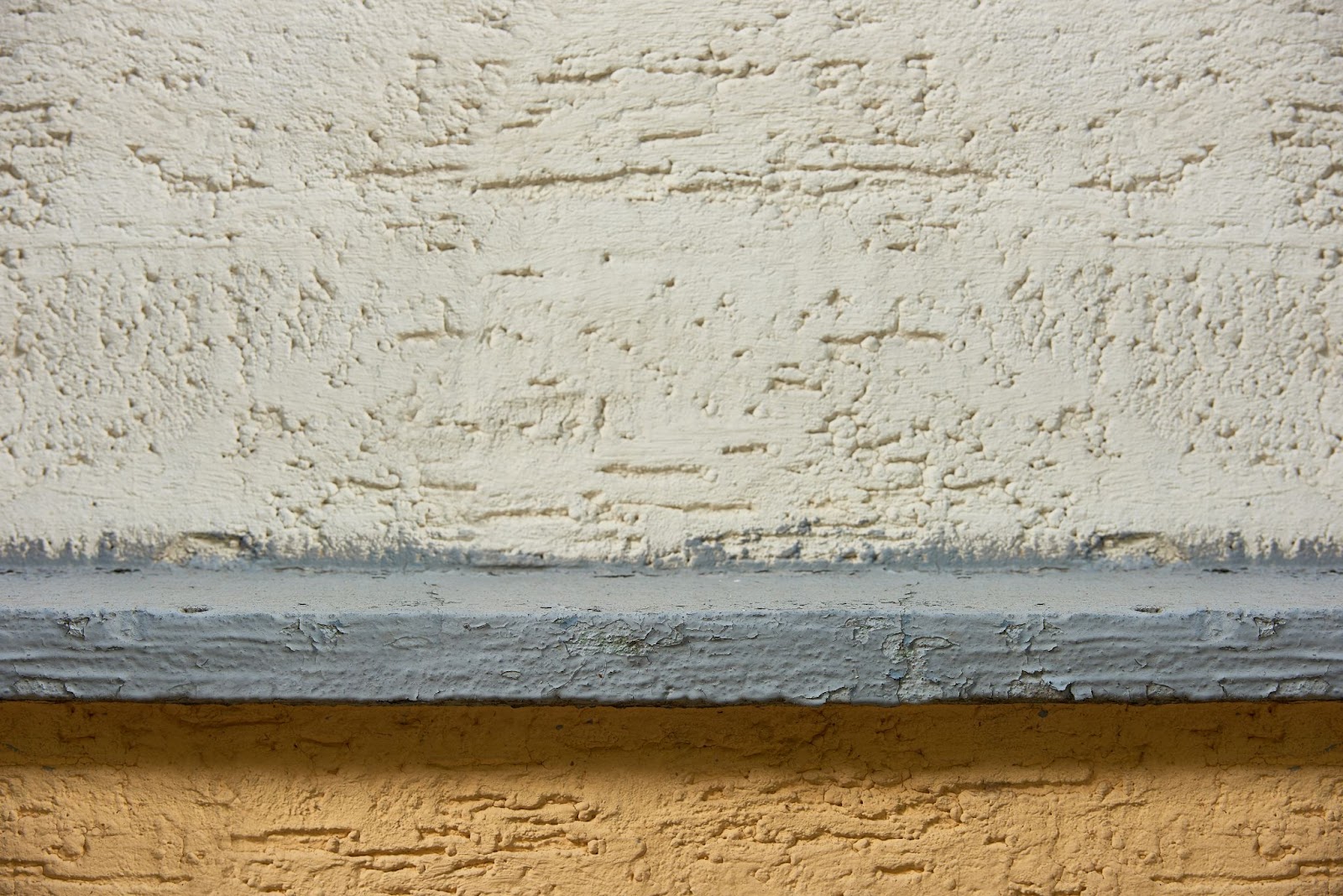 Detailed view of stucco texture on a two-toned concrete wall.