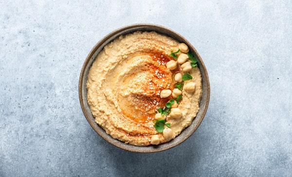 A bowl of creamy hummus topped with whole chickpeas, paprika, sesame seeds, and fresh herbs