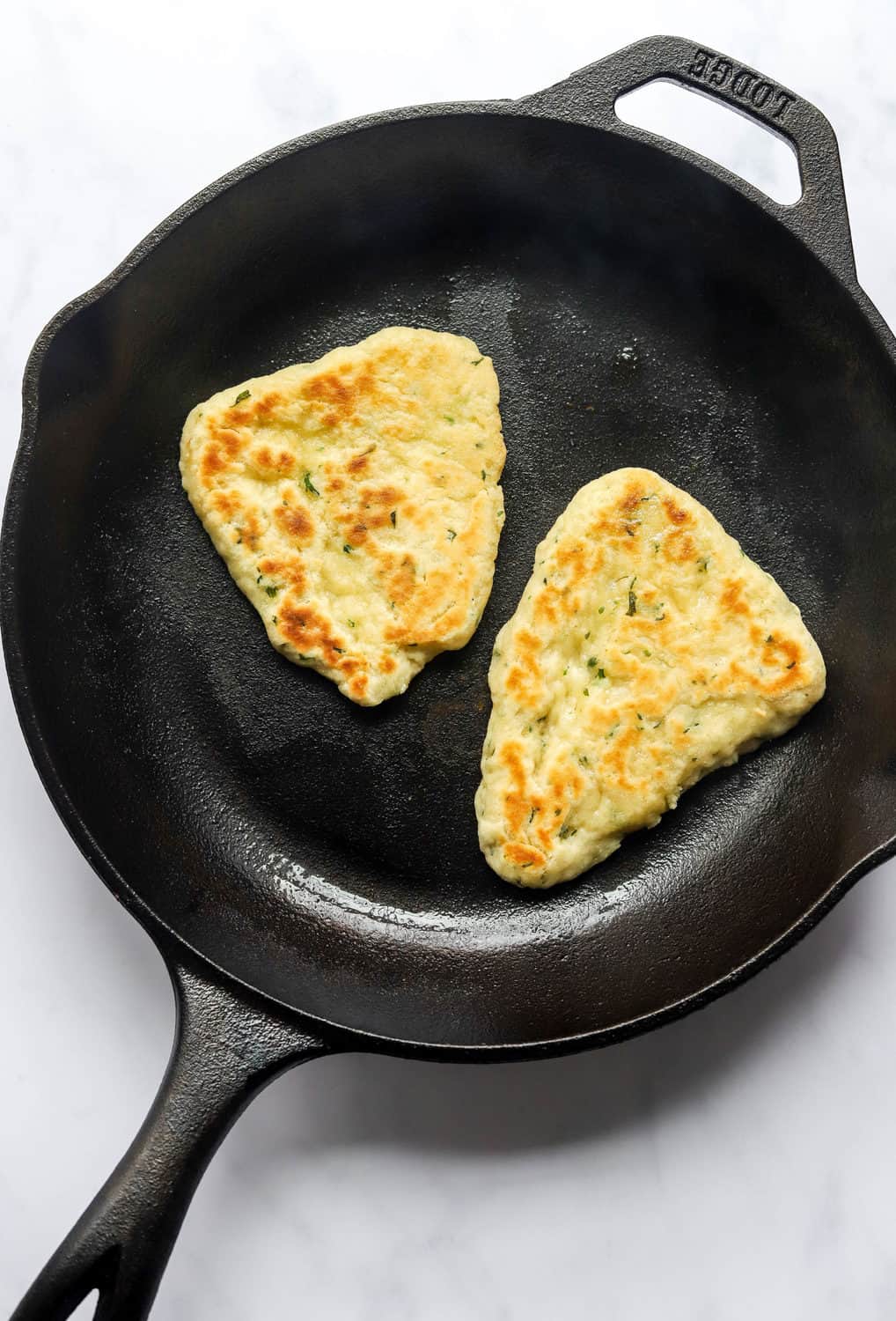 Gluten free naan bread cooking in a cast iron pan.