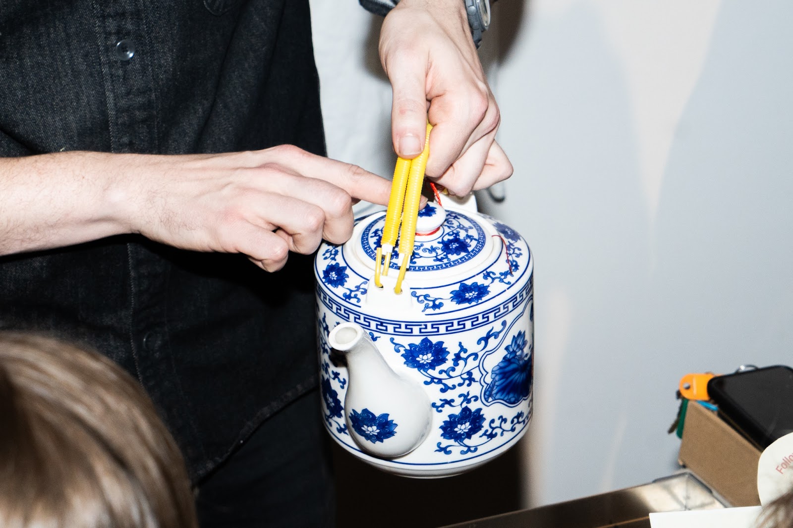 A person ready to pour tea from a traditional Chinese porcelain teapot with blue floral patterns. 