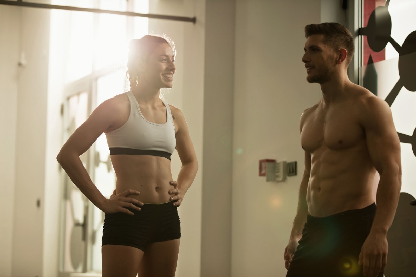 Fit man and woman with toned physiques talking in the gym, representing strength training, fat loss, and muscle retention. This image highlights the benefits of weightlifting and proper nutrition in achieving a lean, athletic body.