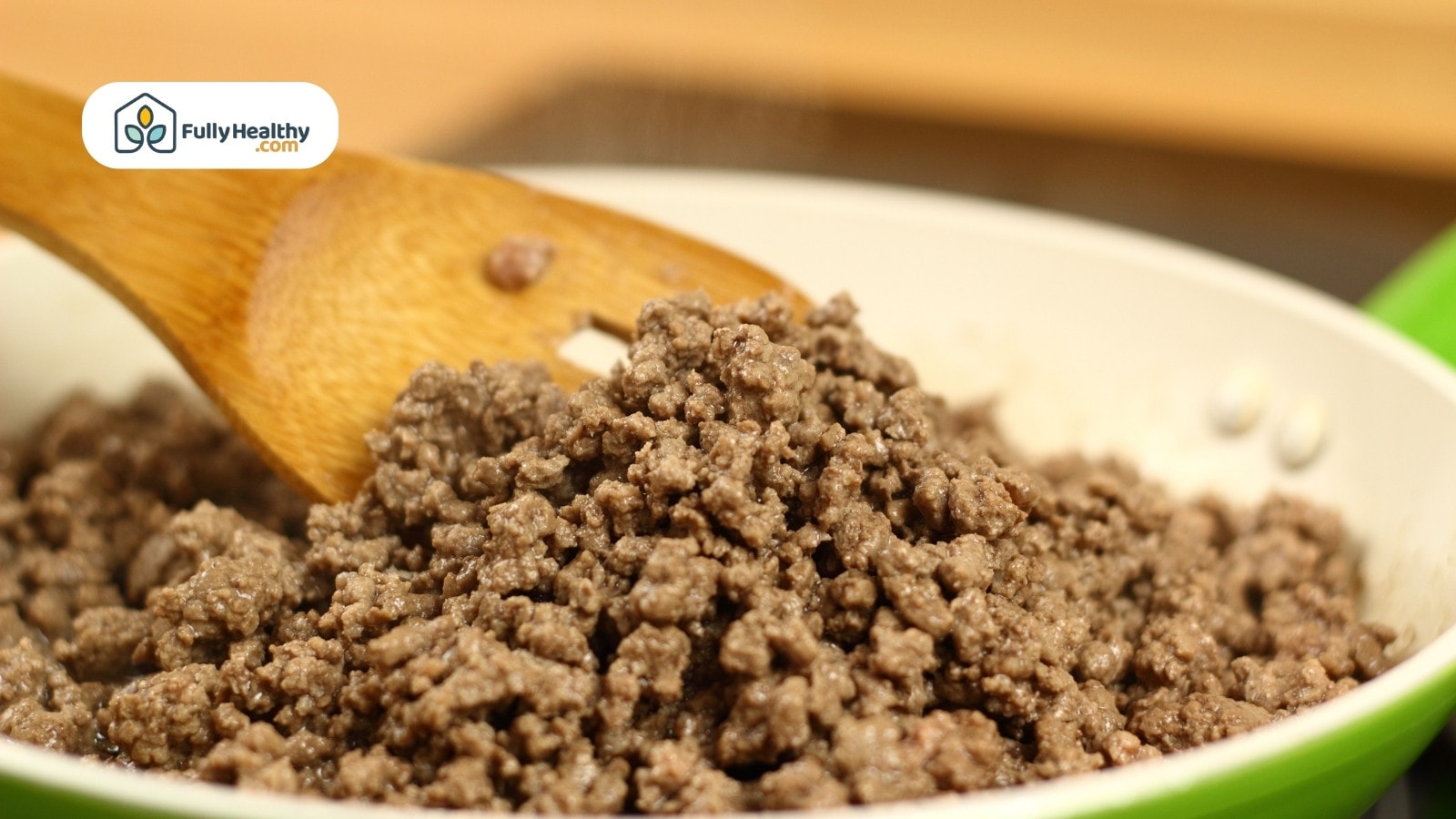 Cooked ground beef in skillet with wooden spoon stirring meat