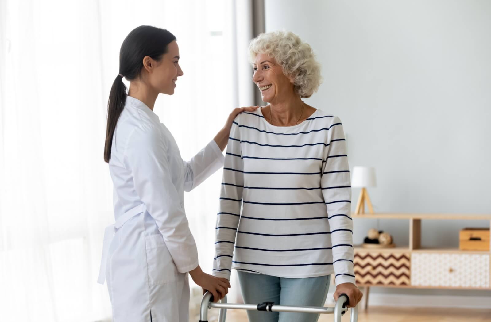 A young physiotherapist helps an older adult adjust their walker to the correct height.