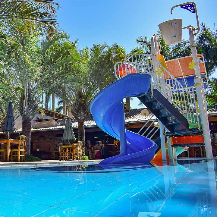 Imagem de uma piscina com um toboágua azul vibrante, cercada por palmeiras e área de lazer, ideal para diversão em família.