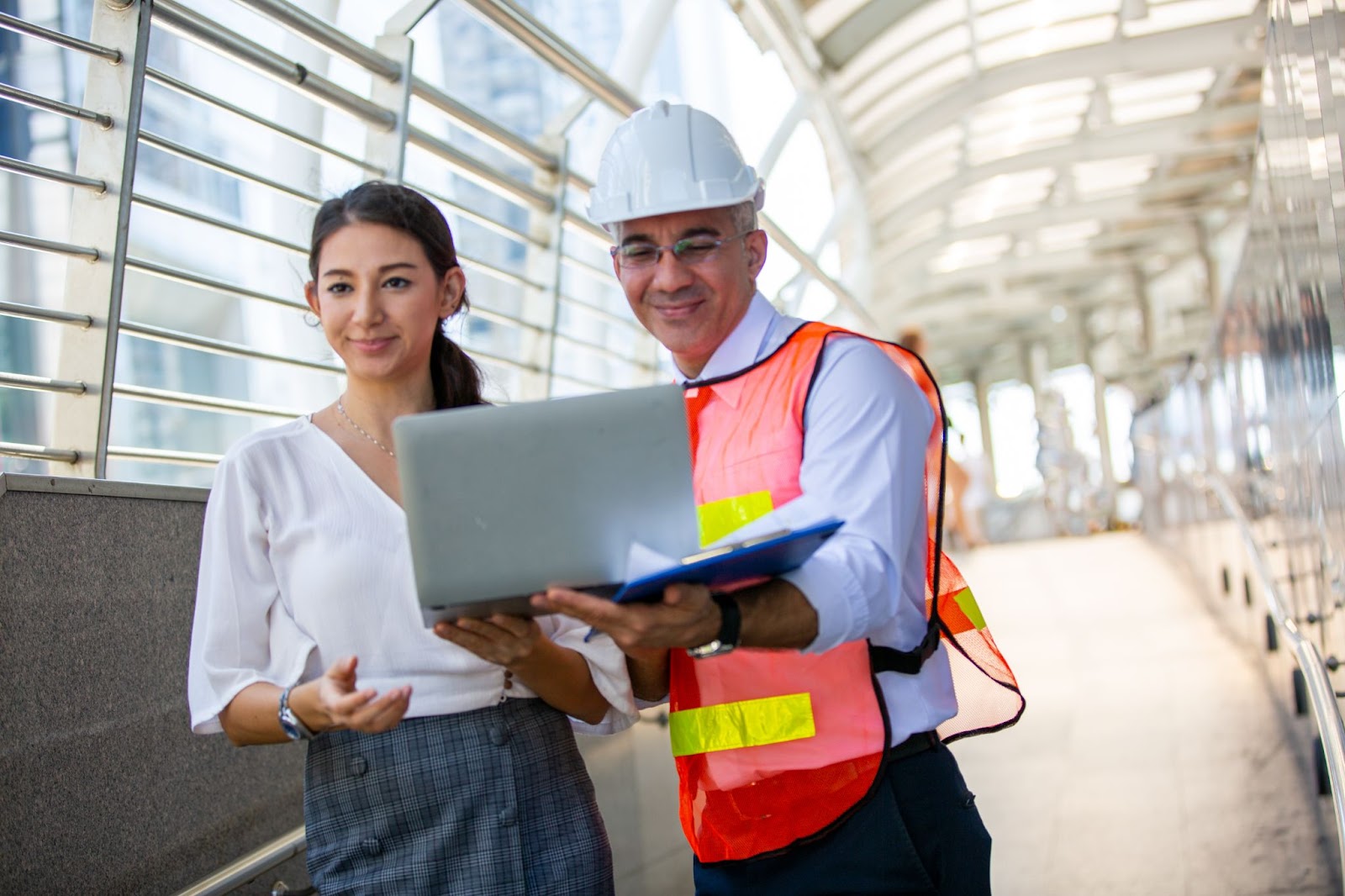 A male engineer uses a laptop to discuss workflow and project plans with his female superior inside a factory.