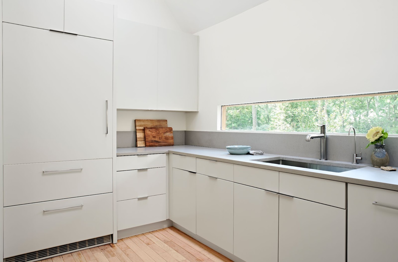 Sunlit kitchen with clean-lined bright white cabinets and matching hidden fridge cabinet.