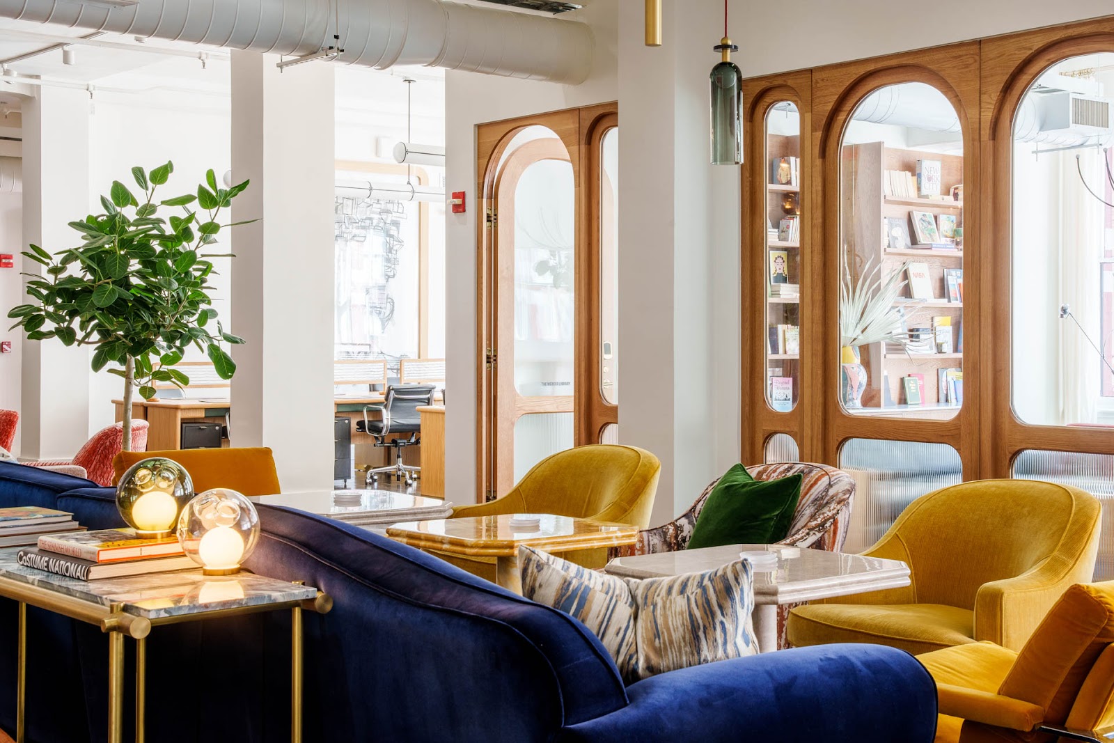 A light-filled office space shows chairs with velvet gold and royal blue chairs and high-gloss tables. 