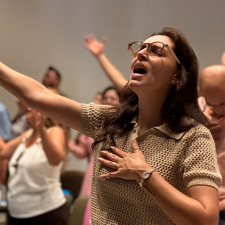 Mulher emocionada em oração ou louvor em um momento religioso, com as mãos ao peito e os olhos fechados, participando de um culto ou culto religioso.