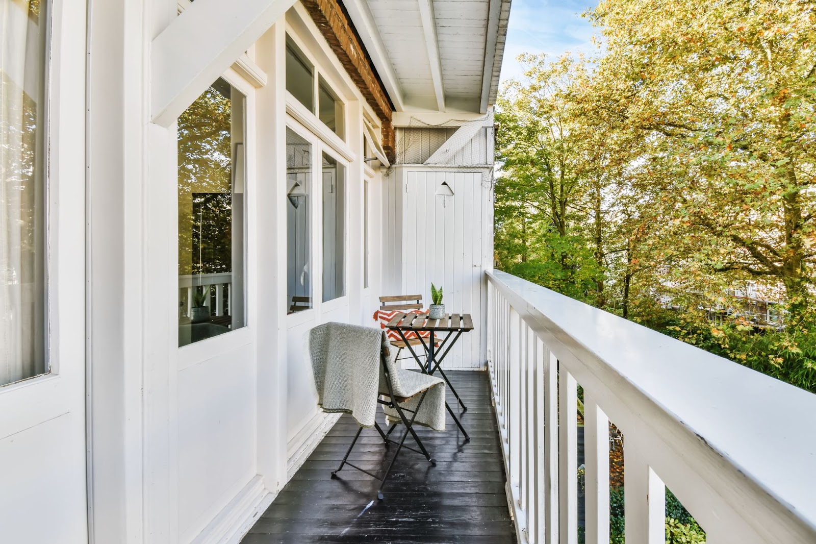 A stunning, elongated white balcony featuring a table and chair set, complemented by elegant and durable white PVC railings.