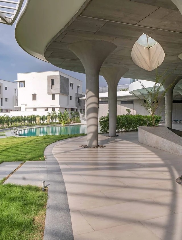 A modern architectural structure with curved, concrete columns and a pergola casting shadows on a walkway—an ideal scene for architectural photography.