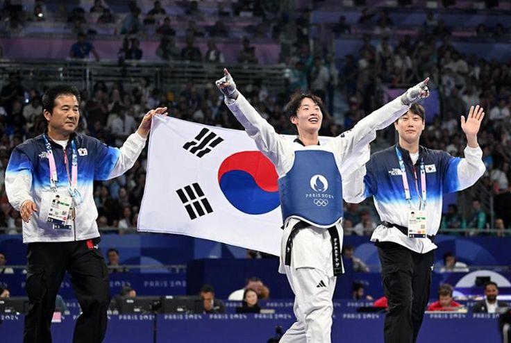 This contain an image of  South Korea martial holding up their flags in front of them as they stand on the ice