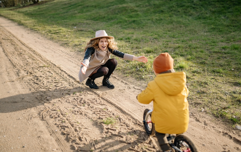 young child riding bike on a dirt road toward mother