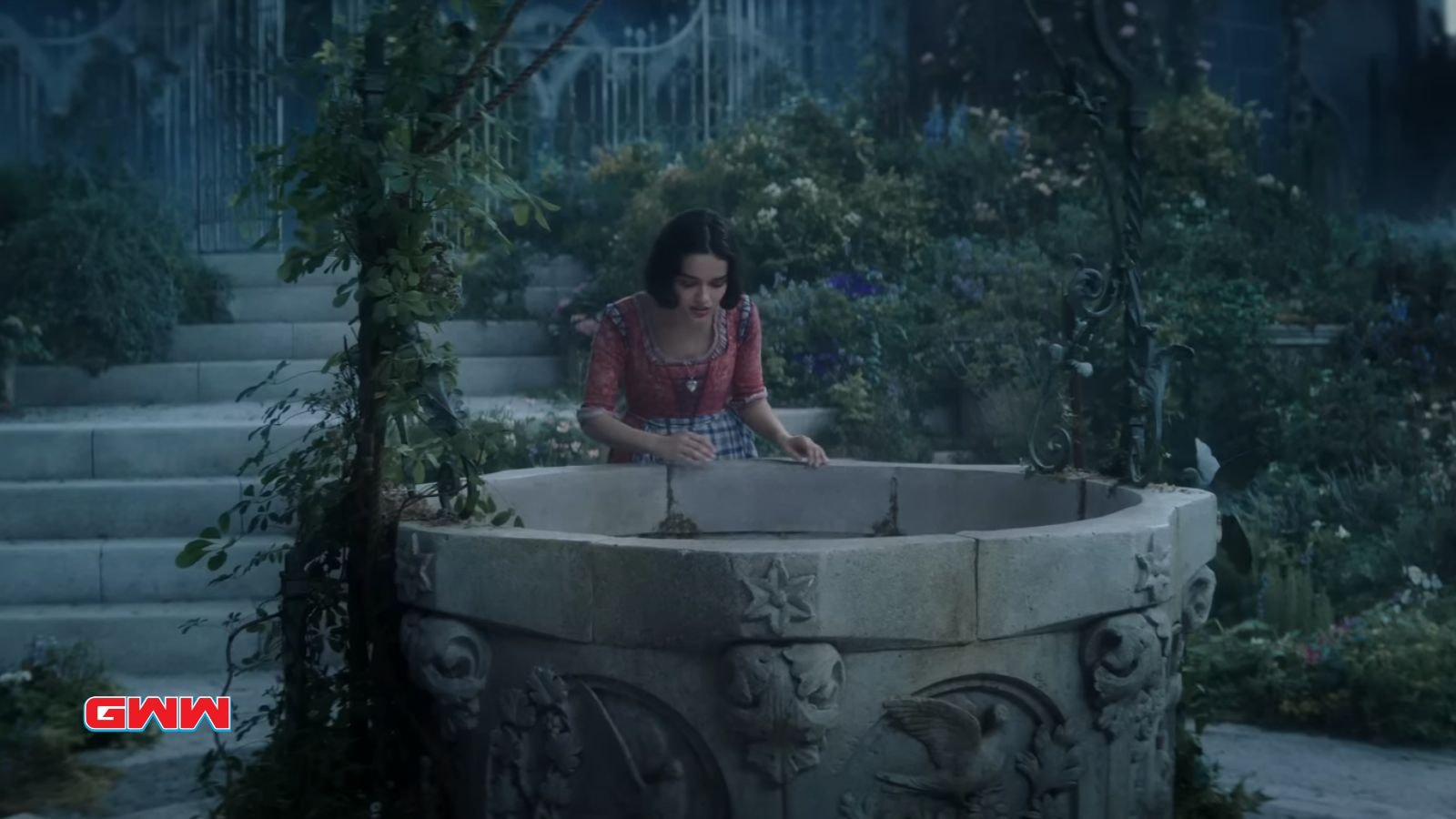 Rachel Zegler as Snow White, standing by a wishing well in a garden.