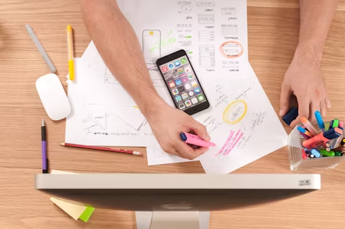 Person highlighting notes on papers with a smartphone and colorful markers on a desk
