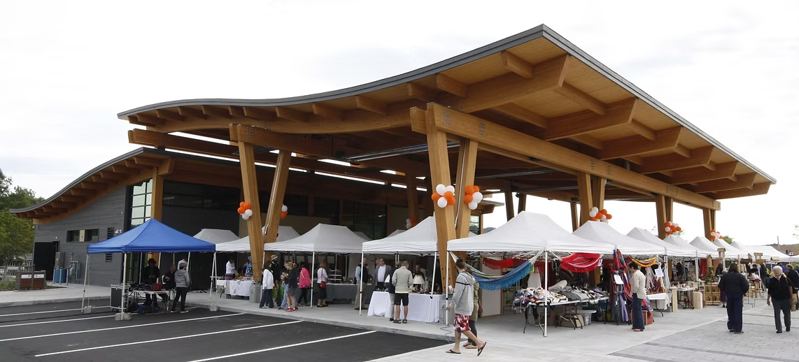 View of the Sainte-Adèle public market under the wooden pavilion, with producers' kiosks and visitors