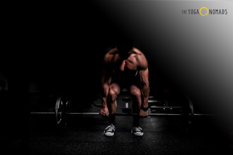 yoga before or after workout? 
The image shows a person in a gym setting preparing to lift a barbell. The environment is dimly lit, highlighting the silhouette of the individual and the barbell