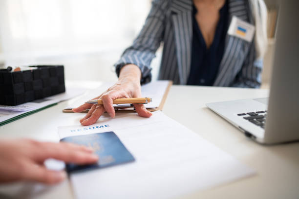 Recruiter reviewing a resume and passport during a job interview at a desk with a laptop.
