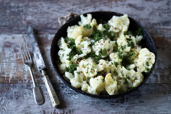 Instant Pot cauliflower served in a dark skillet with vintage-style utensils on a weathered wooden surface