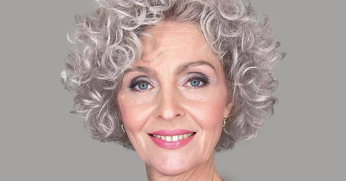 A woman with gray hair styled in cropped curls, showcasing her striking blue eyes and elegant demeanor.