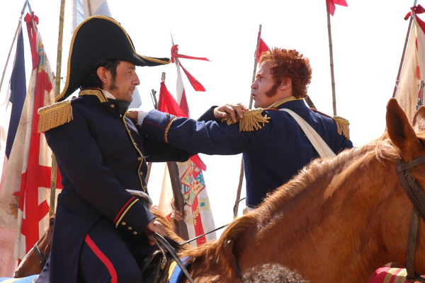 Dos soldados a caballo en uniforme militar durante una confrontación, rodeados de banderas en una recreación de batalla histórica, mostrando un momento tenso de la historia de Chile.