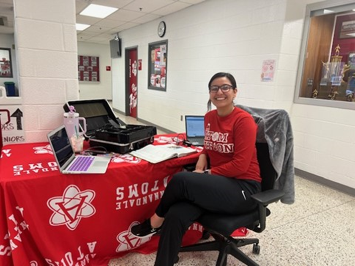 Annandale High School teacher Sandra Benitez sitting at a desk in a school hallway. 