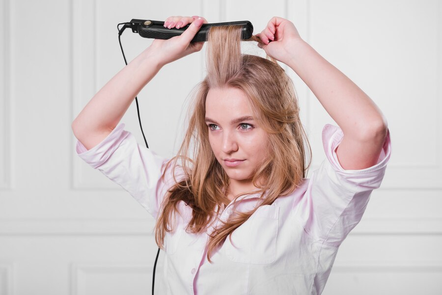 Blonde girl straightening her hair with a straightener