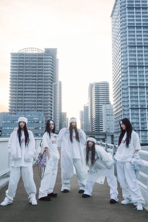 This contain NewJeans  in white outfits standing on a bridge with tall buildings in the background