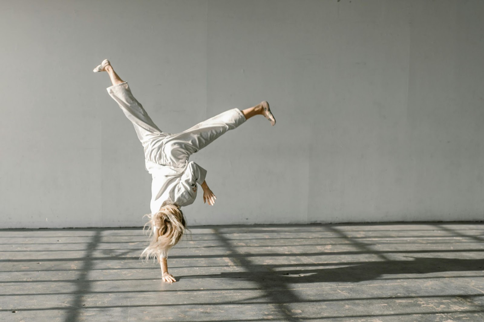 A martial arts student in a white gi performing a dynamic flip, with one hand on the floor and their body suspended mid-air