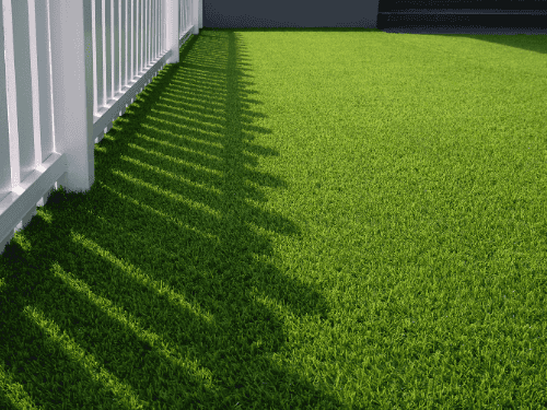 Artificial turf cost calculator example: clean synthetic lawn installation beside white fence in residential backyard
