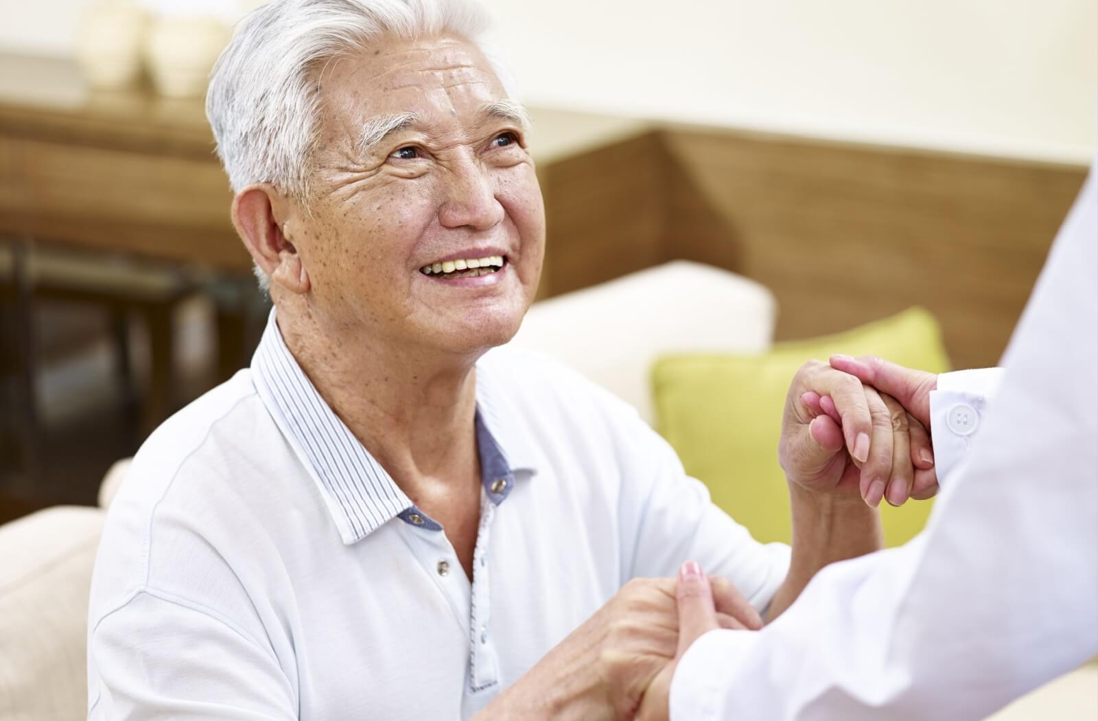 Smiling senior man holding hands with a caregiver in a supportive home setting.