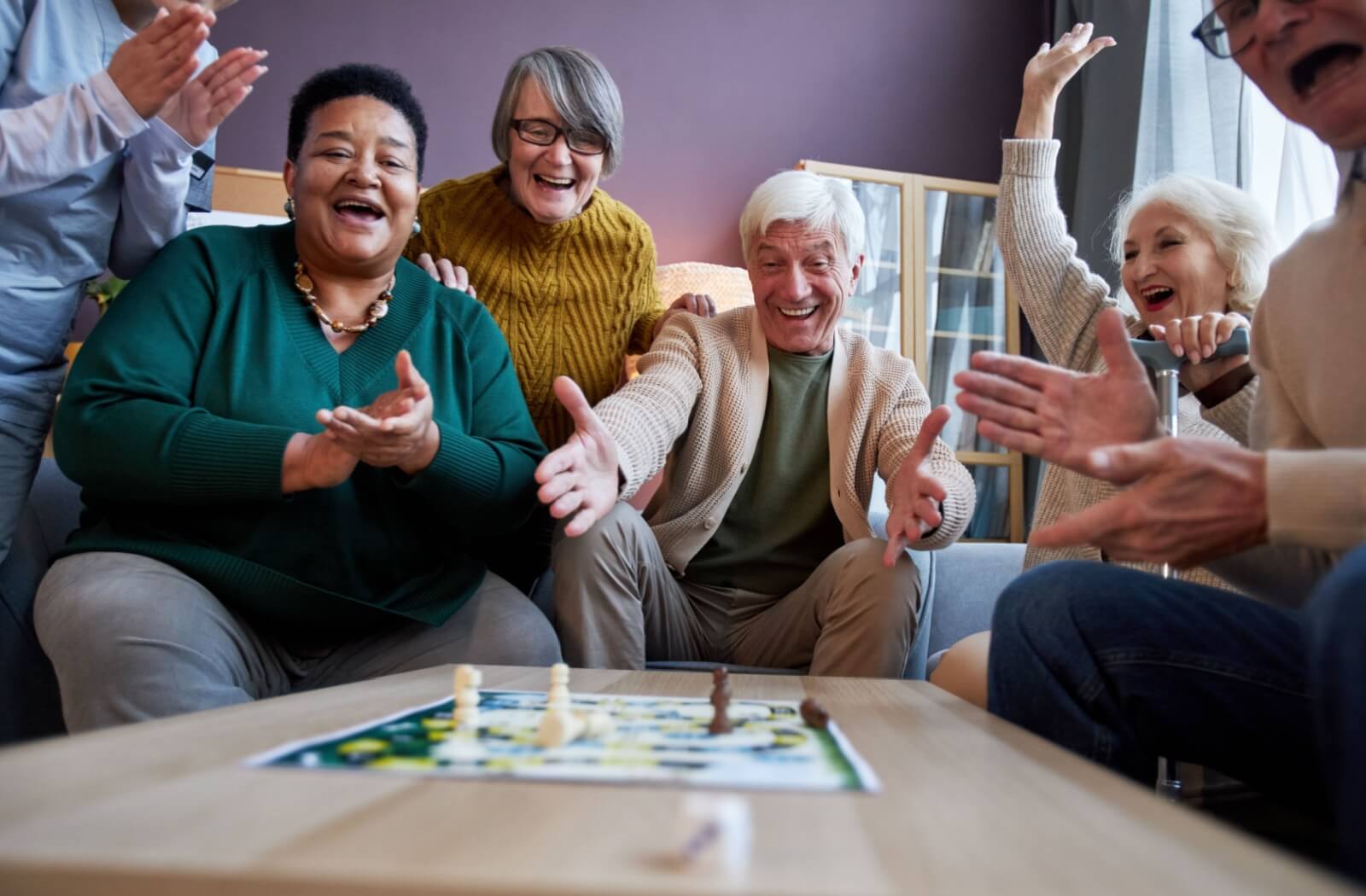 A group of seniors cheer as they play a boardgame together at a senior living community.
