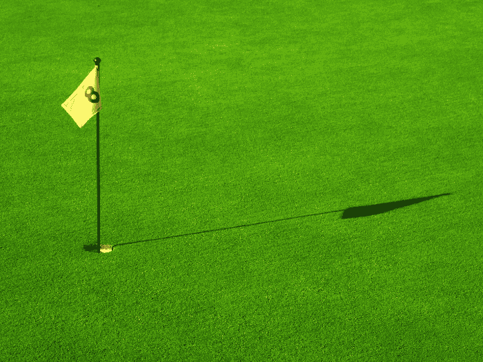 Artificial turf putting green with hole and flagstick casting a shadow on a bright green surface