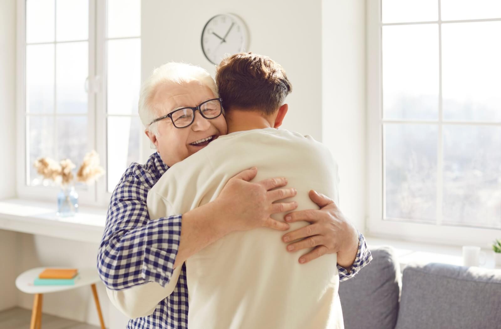 An adult son hugging his senior father while he visits him at his home in an assisted living community.