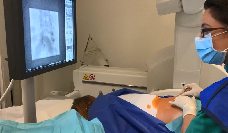 Photo d'une médecin radiologue en train d'effectuer une infiltration dans le bas du dos d'une patiente sous contrôle radiographique