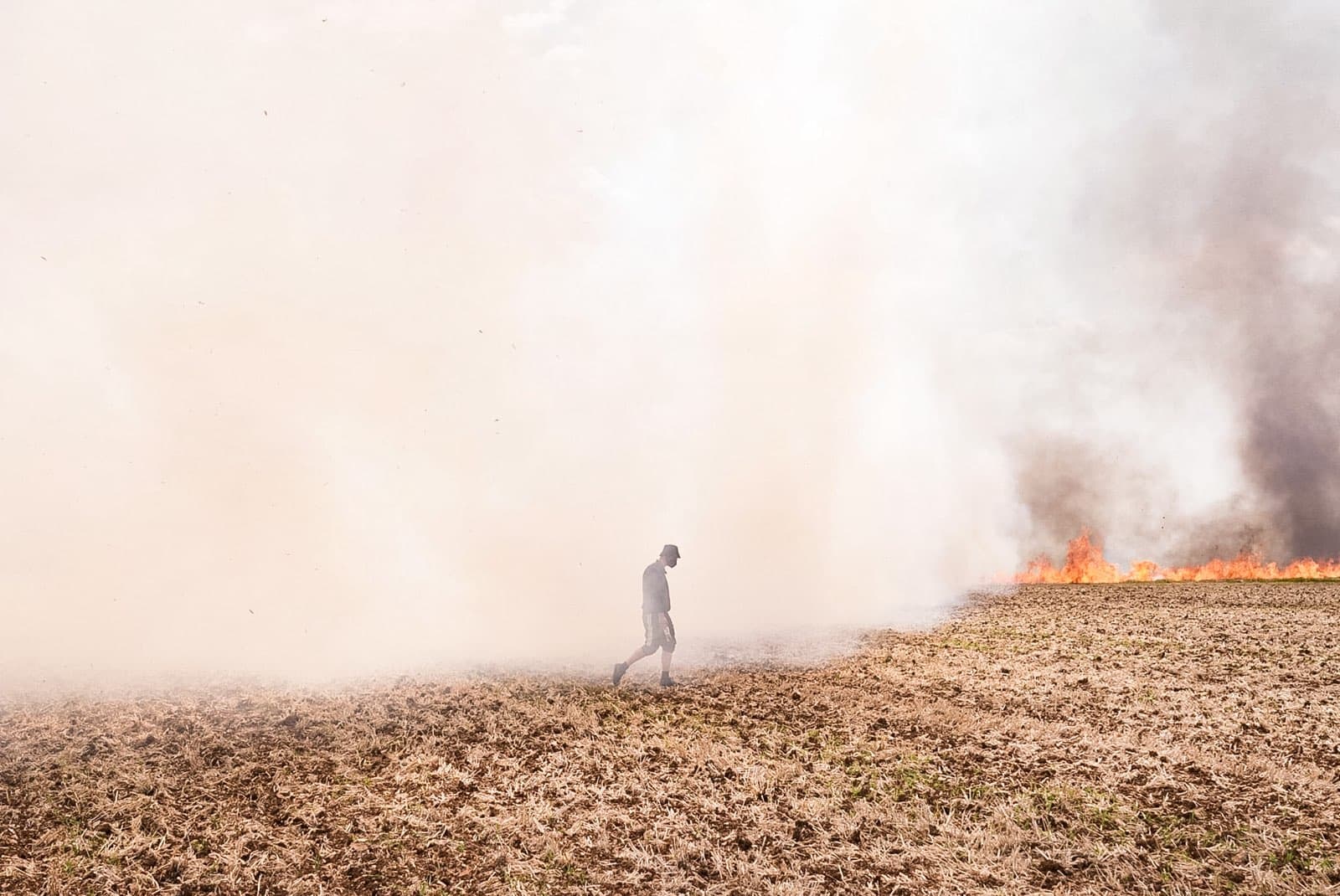 A lone protester wearing a gas mask walks through a huge cloud of smoke over a burning field