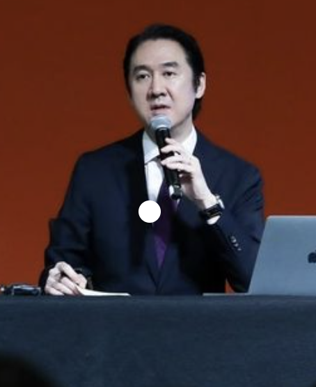 A picture of HYBE CCO on a black suit holding a microphone on his hand 