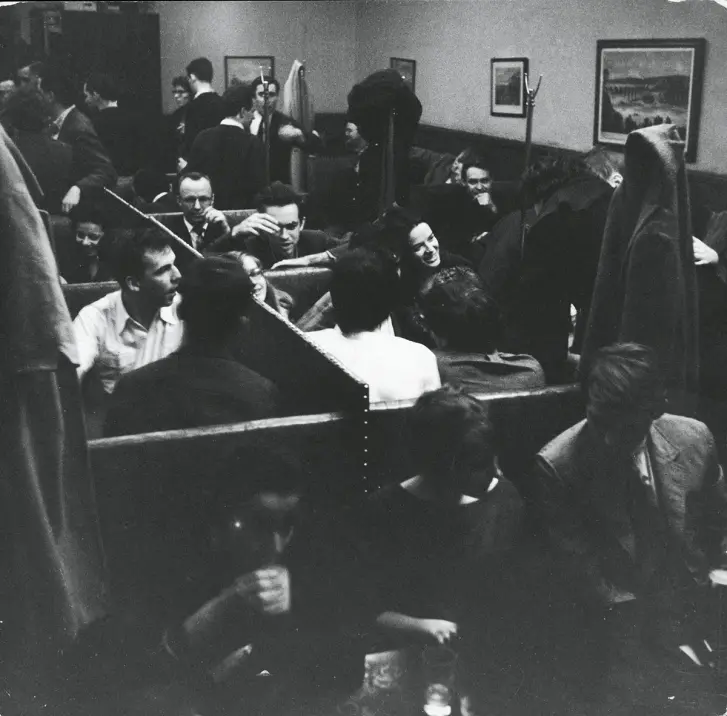 Black and white photo of the Cedar Tavern in the 1950s, a legendary Greenwich Village bar packed with artists, writers, and poets. The crowded, smoky scene shows patrons in booths and at tables, capturing the vibrant social atmosphere that made the Cedar Tavern a hub for Abstract Expressionist painters like Jackson Pollock, Willem de Kooning, and Mark Rothko, as well as Beat Generation writers such as Jack Kerouac and Allen Ginsberg. This iconic New York City bar was a central meeting place for avant-garde creatives, fostering the exchange of ideas that shaped mid-century American art and literature.