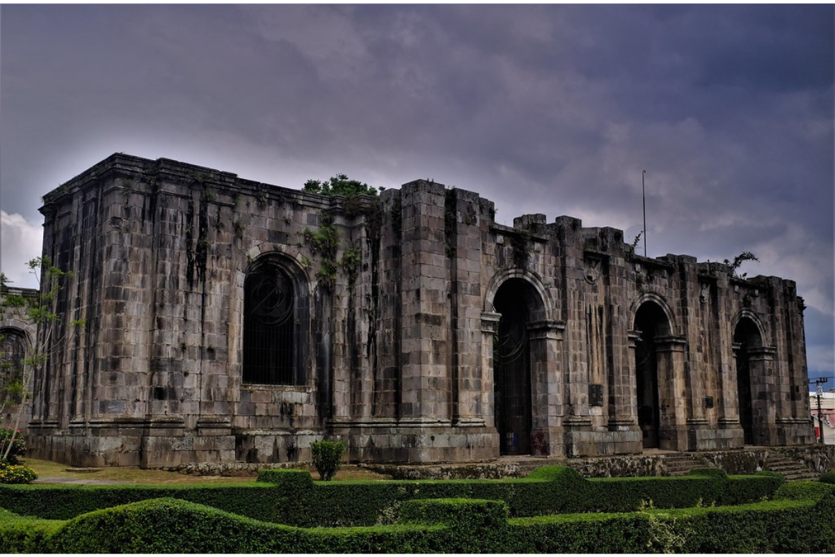 There is a border of green plants around the old church in Cartago