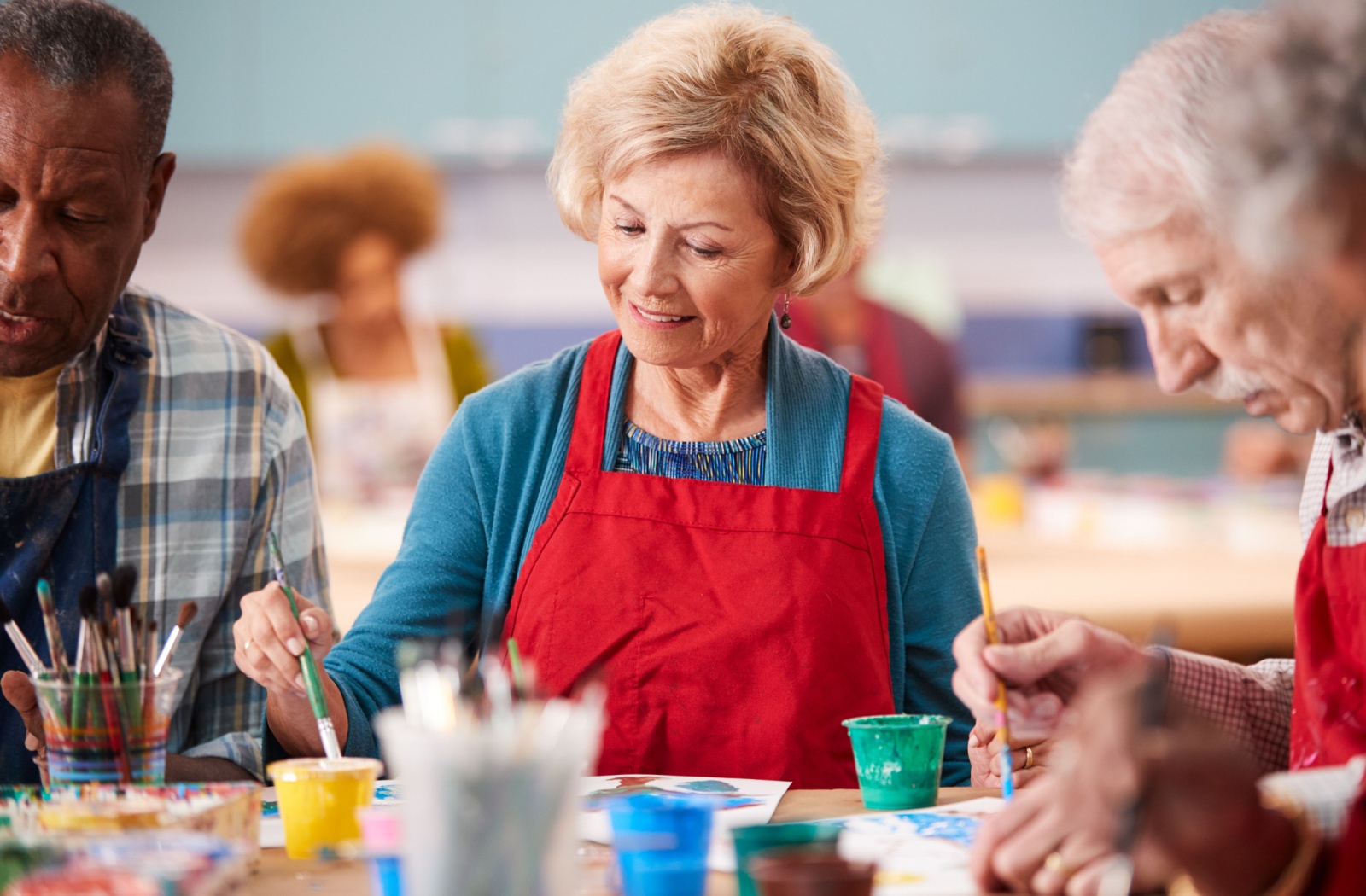 A group of older adults smile and paint at their memory care community