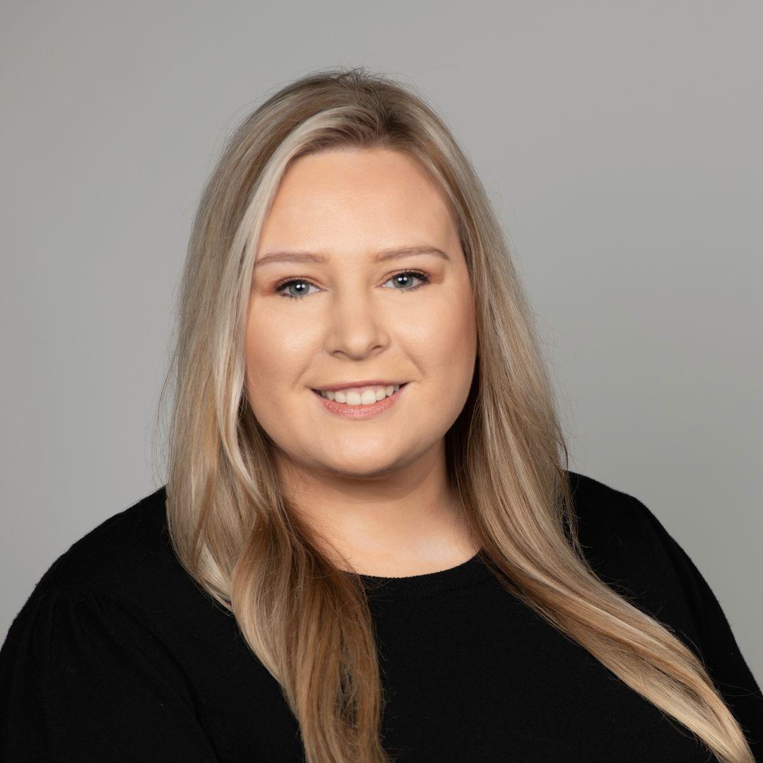 Corporate headshot of a woman with long blonde hair and a black top, taken by a corporate headshot photographer.